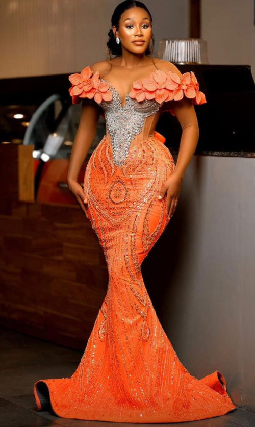 Woman wearing an orange evening gown with floral details indoors.